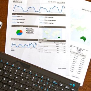 Flatlay of a business analytics report, keyboard, pen, and smartphone on a wooden desk.